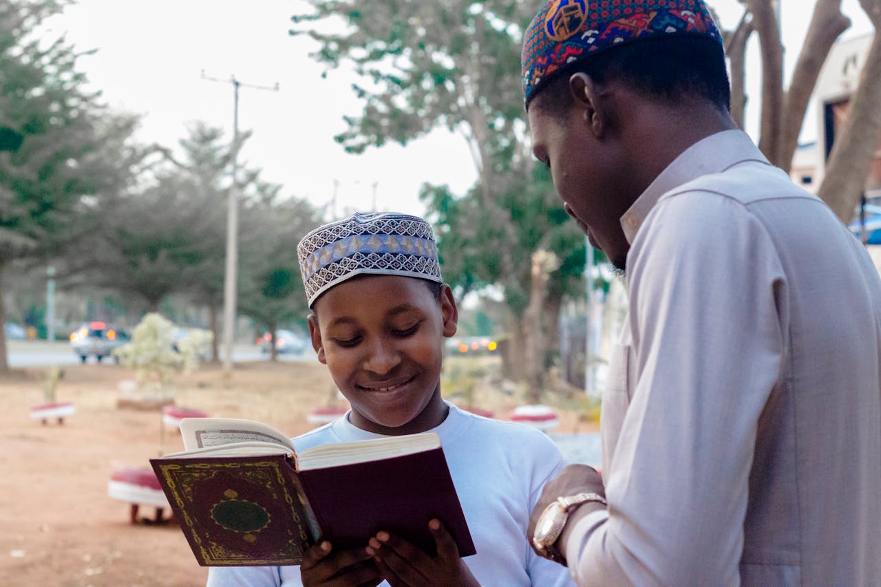 Services Young boy and man reading a religious book together while smiling, outdoors.