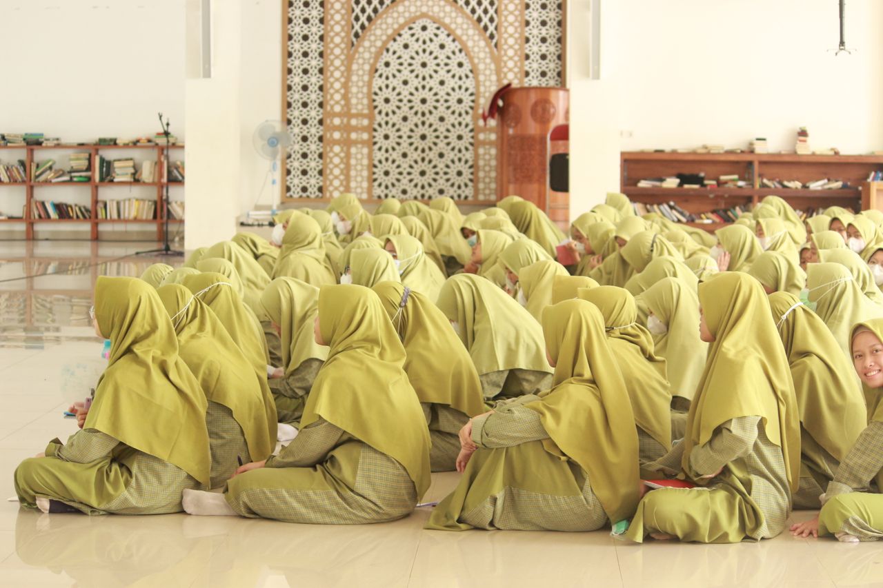 Services A group of women in hijabs sitting on the mosque's tiled floor, engaged in prayer.